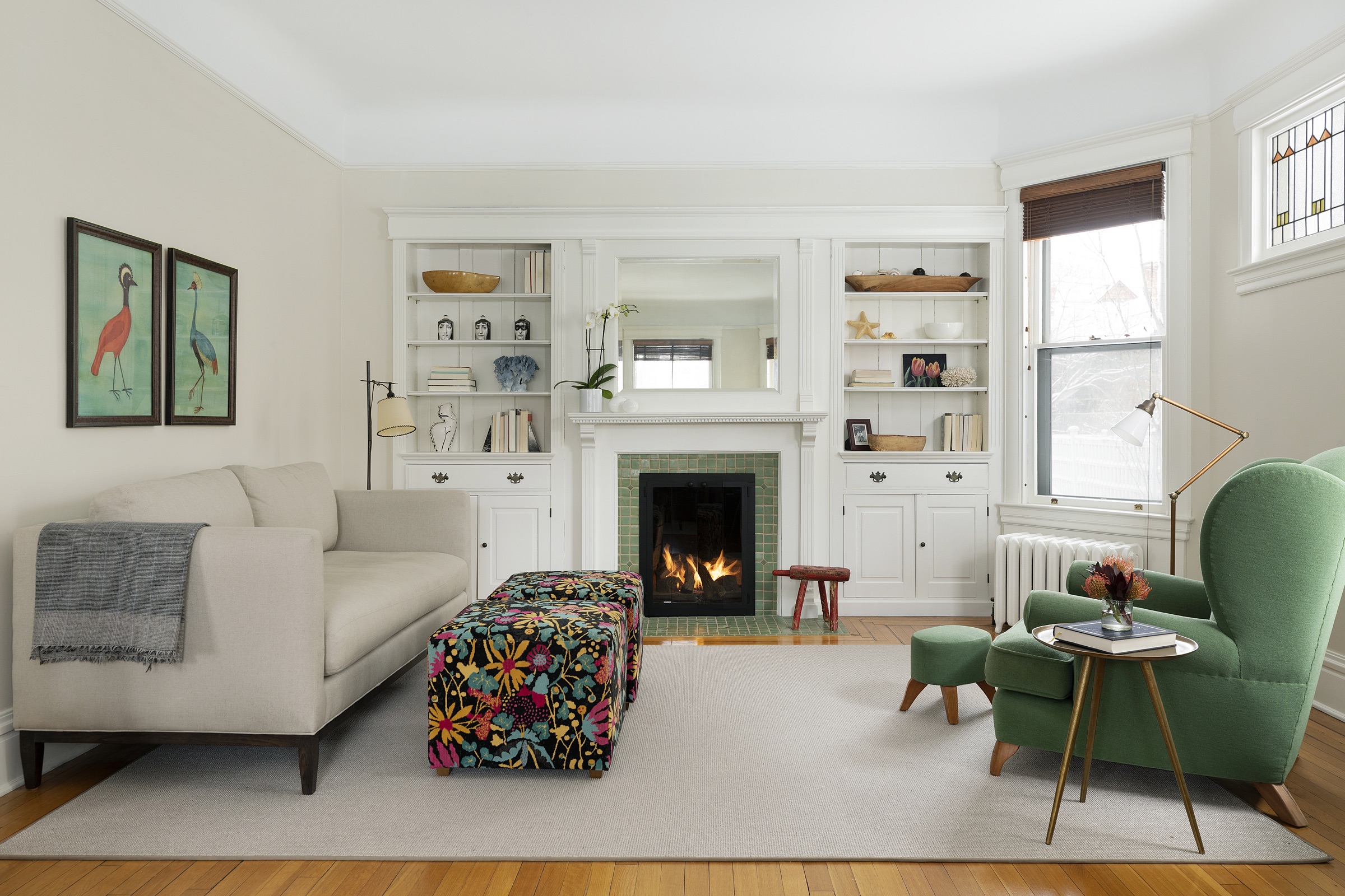 Living room with green tile fireplace, painted built-ins and a floral ottoman in a 100-year-old Lowry Hill home.