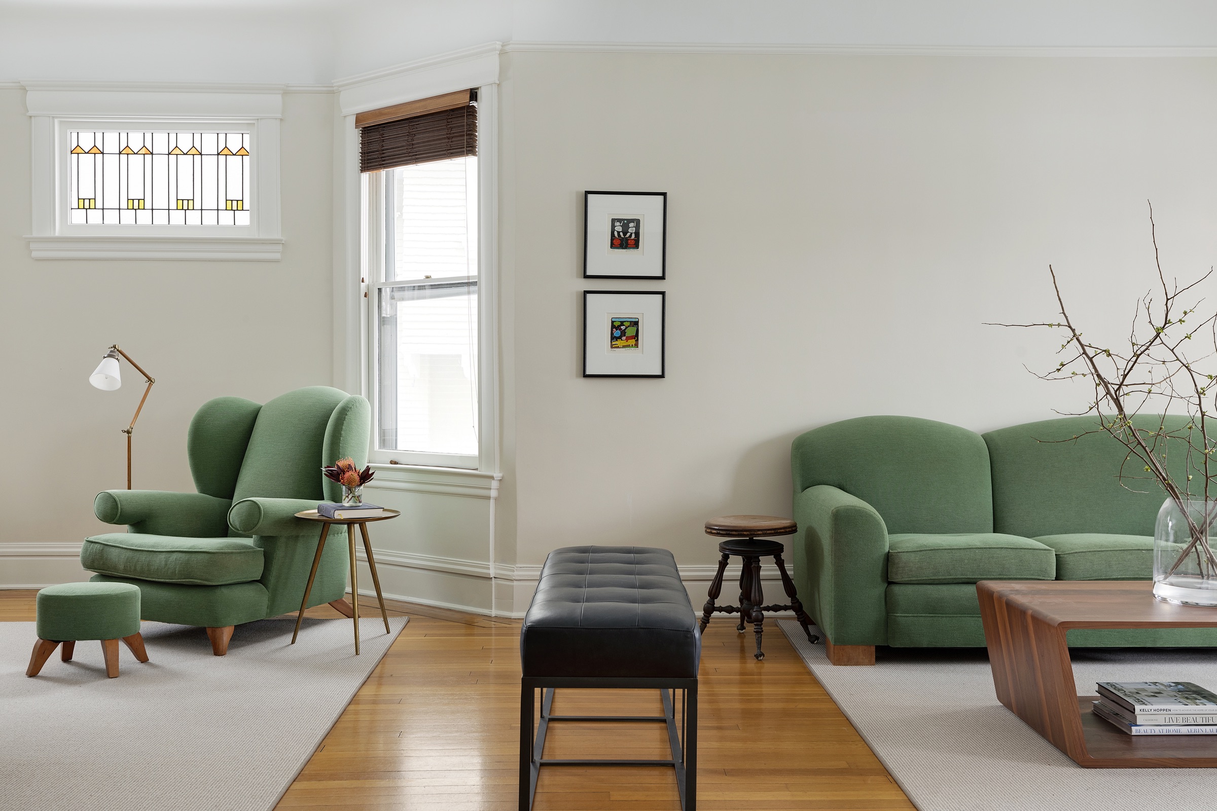 Living room with green wingback chair, curved green sofa and original stained glass window in Lowry Hill.