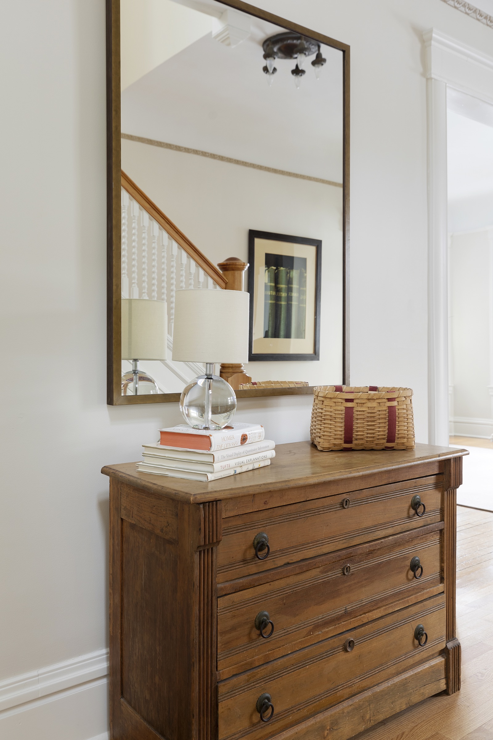 Entry vignette with antique wood chest, brass-framed mirror and a lamp in this Lowry Hill Minneapolis home.